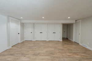 Unfurnished bedroom with multiple closets, a textured ceiling, and light wood-type flooring