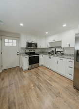 Kitchen featuring stainless steel appliances, white cabinetry, light wood-type flooring, and light stone counters