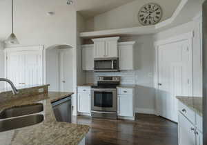 Kitchen with sink, decorative light fixtures, appliances with stainless steel finishes, light stone countertops, and white cabinets