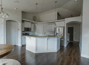 Kitchen with stainless steel appliances, decorative light fixtures, a center island with sink, and white cabinets