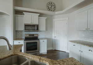 Kitchen featuring sink, white cabinetry, light stone counters, appliances with stainless steel finishes, and decorative backsplash