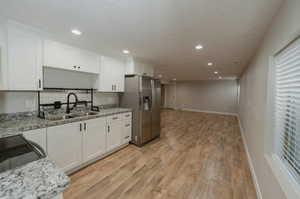 Kitchen with sink, light stone countertops, white cabinets, and stainless steel refrigerator with ice dispenser