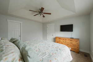 Bedroom featuring ceiling fan, carpet flooring, and a raised ceiling