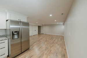 Kitchen featuring white cabinetry, stainless steel refrigerator with ice dispenser, light stone countertops, and light hardwood / wood-style floors