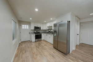 Kitchen with appliances with stainless steel finishes, white cabinetry, sink, light hardwood / wood-style floors, and a textured ceiling