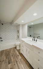 Full bathroom with toilet, vanity, tiled shower / bath combo, a fireplace, and hardwood / wood-style floors