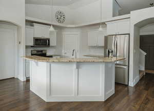 Kitchen with white cabinetry, an island with sink, hanging light fixtures, light stone counters, and stainless steel appliances