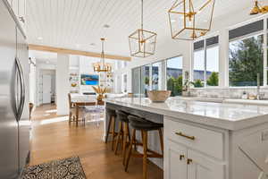 Kitchen featuring light stone counters, wood ceiling, a chandelier, built in fridge, and white cabinets