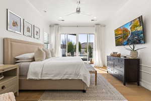 Bedroom featuring ceiling fan, a textured ceiling, access to exterior, and light hardwood / wood-style floors