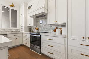 Kitchen featuring premium range hood, stainless steel range with electric stovetop, dark hardwood / wood-style floors, tasteful backsplash, and white cabinets