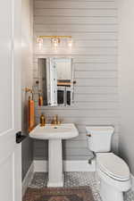 Bathroom with wooden walls, sink, tile patterned flooring, toilet, and washing machine and dryer