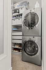 Laundry room featuring stacked washer and dryer and light colored carpet