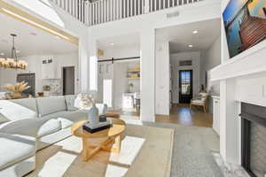 Living room with a notable chandelier, a towering ceiling, light hardwood / wood-style floors, and a barn door