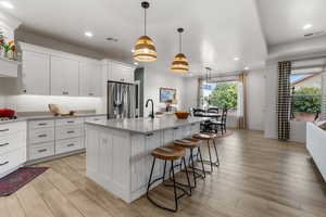 Kitchen with a breakfast bar, white cabinetry, stainless steel fridge with ice dispenser, hanging light fixtures, and a kitchen island with sink