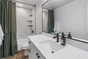 Full bathroom with hardwood / wood-style flooring, vanity, shower / bath combination with curtain, and toilet