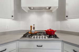 Kitchen featuring white cabinetry, stainless steel gas cooktop, and custom range hood