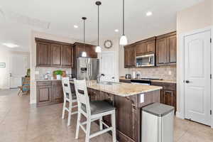 Kitchen featuring sink, appliances with stainless steel finishes, pendant lighting, light stone countertops, and a kitchen island with sink