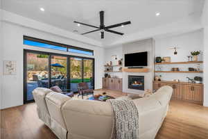 Living room with french doors, a large fireplace, ceiling fan, and light hardwood / wood-style floors