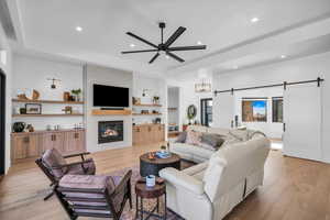 Living room featuring built in shelves, light hardwood / wood-style flooring, a large fireplace, ceiling fan, and a barn door