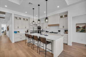 Kitchen with appliances with stainless steel finishes, pendant lighting, a center island with sink, and white cabinets