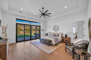 Bedroom with access to exterior, light hardwood / wood-style floors, and a raised ceiling