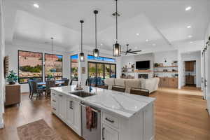 Kitchen featuring pendant lighting, white cabinetry, a kitchen island with sink, light stone counters, and stainless steel dishwasher