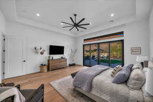 Bedroom featuring hardwood / wood-style floors, access to outside, ceiling fan, a raised ceiling, and french doors