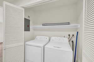 Washroom with hardwood / wood-style flooring, electric panel, and washing machine and clothes dryer