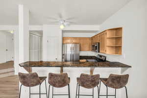 Kitchen featuring appliances with stainless steel finishes, dark stone countertops, ceiling fan, kitchen peninsula, and light wood-type flooring