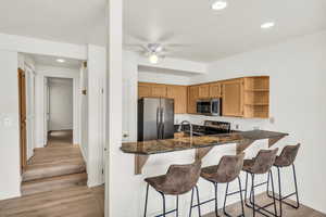 Kitchen featuring ceiling fan, stainless steel appliances, light hardwood / wood-style floors, kitchen peninsula, and dark stone counters