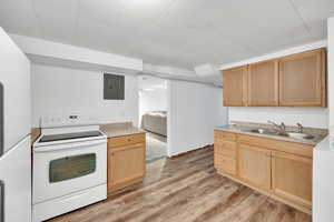 Kitchen with electric stove, sink, electric panel, light hardwood / wood-style floors, and light brown cabinetry