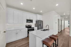 Kitchen with appliances with stainless steel finishes, white cabinetry, an island with sink, sink, and a breakfast bar area