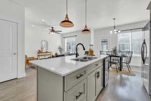 Kitchen featuring sink, hanging light fixtures, stainless steel appliances, a center island with sink, and light wood-type flooring