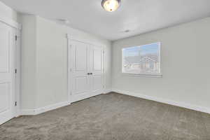 Unfurnished bedroom with light colored carpet, a closet, and a textured ceiling