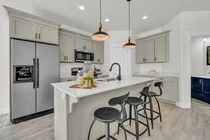 Kitchen with appliances with stainless steel finishes, sink, a center island with sink, and gray cabinetry