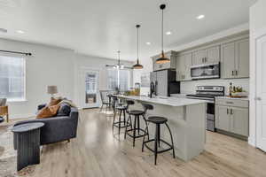 Kitchen featuring gray cabinets, appliances with stainless steel finishes, a wealth of natural light, an island with sink, and decorative light fixtures