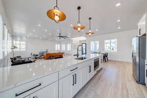 Kitchen with sink, stainless steel fridge, white cabinetry, hanging light fixtures, and light stone countertops