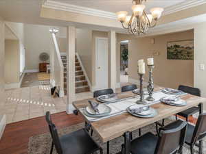 Dining space with ornamental molding, a tray ceiling, a chandelier, and light hardwood / wood-style floors