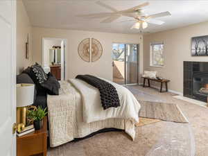 Carpeted bedroom featuring a tile fireplace, access to exterior, ceiling fan, and ensuite bath