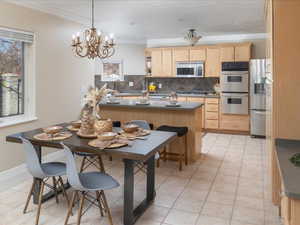 Kitchen with appliances with stainless steel finishes, light brown cabinetry, sink, backsplash, and crown molding