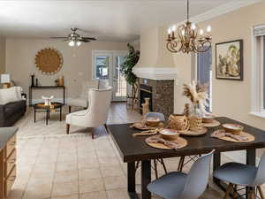 Dining space with crown molding, a high end fireplace, light tile patterned flooring, ceiling fan with notable chandelier, and french doors