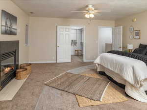 Carpeted bedroom with ceiling fan, a fireplace, and a textured ceiling