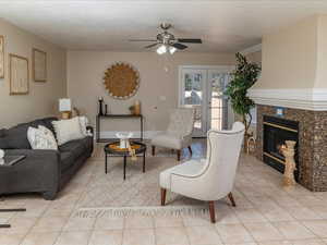 Tiled living room featuring ceiling fan, a premium fireplace, a textured ceiling, and french doors