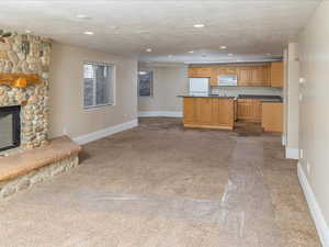 Kitchen featuring light brown cabinetry, a textured ceiling, a fireplace, and white appliances