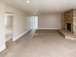 Unfurnished living room featuring a fireplace, light colored carpet, and a textured ceiling