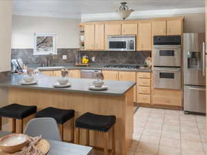 Kitchen featuring light brown cabinetry, sink, a breakfast bar area, appliances with stainless steel finishes, and kitchen peninsula