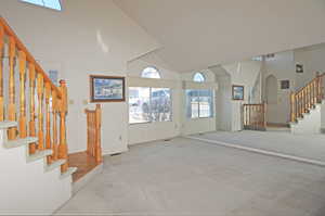 Unfurnished living room featuring high vaulted ceiling and light carpet