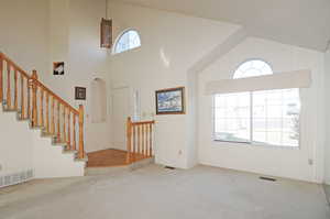 Unfurnished living room with light carpet and high vaulted ceiling