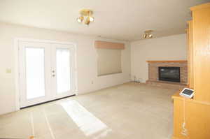 Unfurnished living room featuring light carpet, a brick fireplace, and french doors