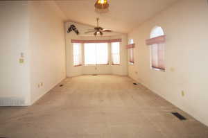 Carpeted empty room featuring lofted ceiling and ceiling fan